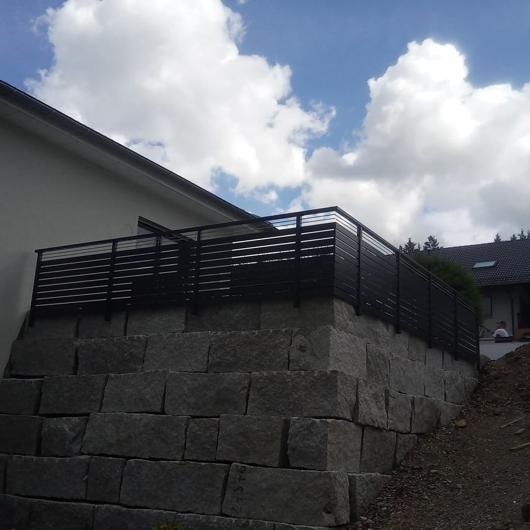 Schwarzes Querlattengeländer auf einer Natursteinmauer